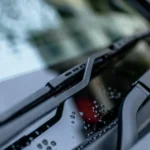 Driver comparing beam and conventional wiper blades beside a wet car windshield