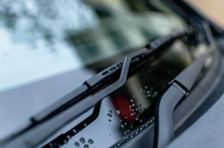 Driver comparing beam and conventional wiper blades beside a wet car windshield