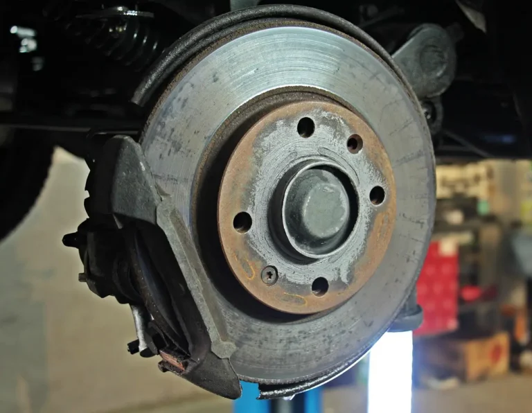 Mechanic inspecting a car brake rotor and caliper in a sunlit repair shop