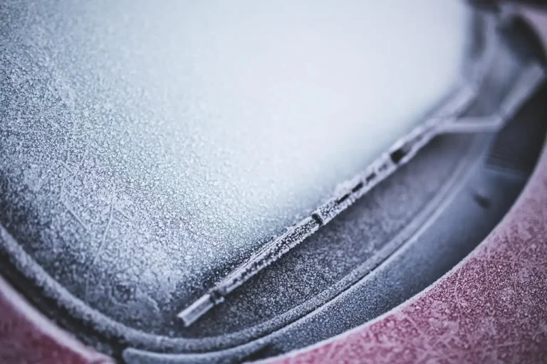 Person measuring a windshield wiper blade beside a sedan in daylight.