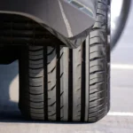 Person examining a car tire sidewall beside a parked vehicle in daylight