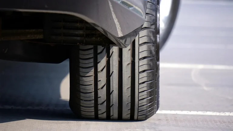 Person examining a car tire sidewall beside a parked vehicle in daylight