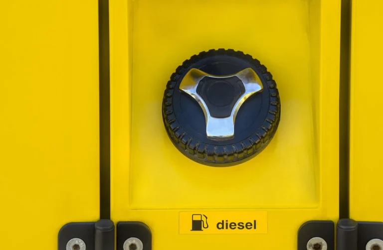 Driver checking a loose gas cap beside an open fuel filler on a sedan at a gas station.