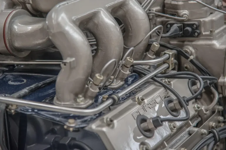 Mechanic holding a used spark plug beside an open car engine in a garage