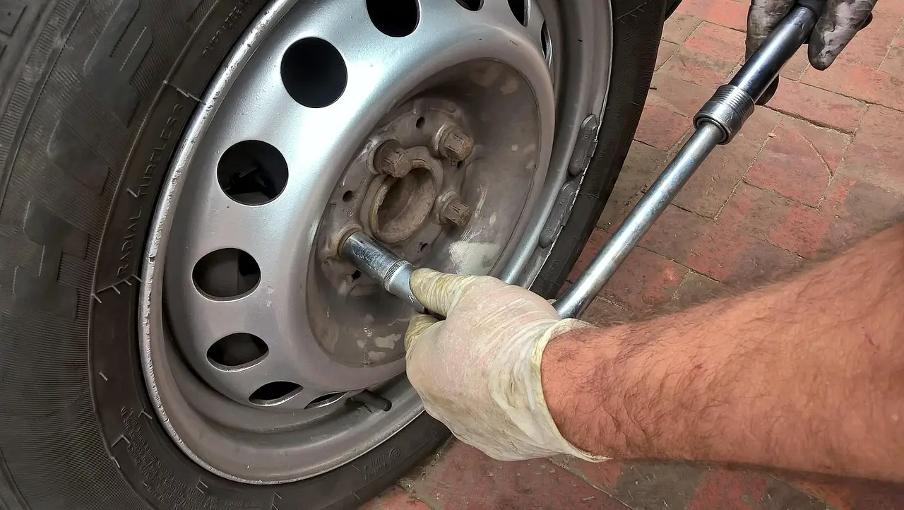 Driver and technician inspect a car tire beside a sedan in natural daylight