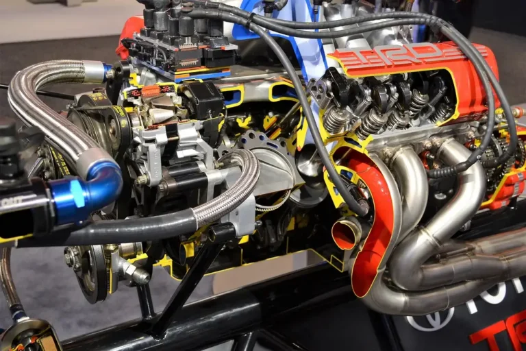 Car engine bay with visible fuel injectors and a mechanic’s hands pointing at them