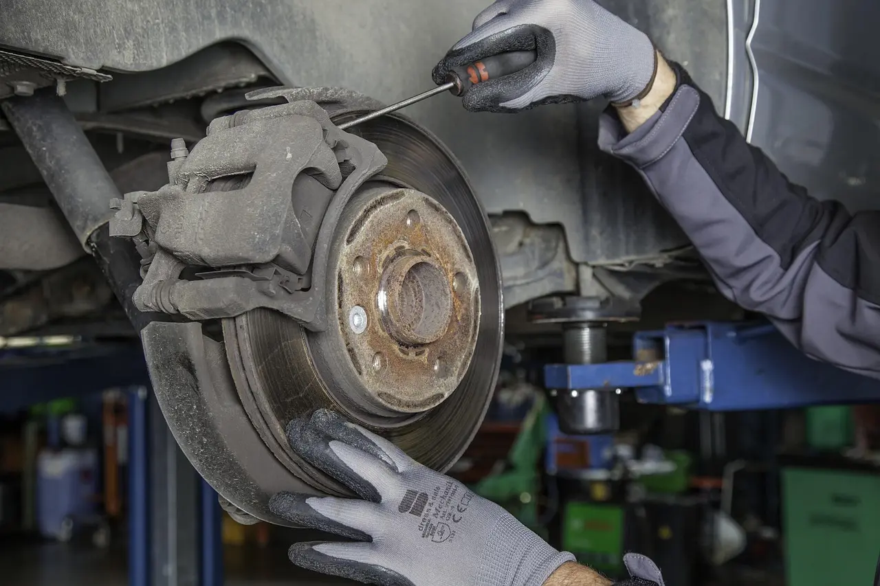 Mechanic and driver inspect a car's front brake rotor and caliper in a repair bay.