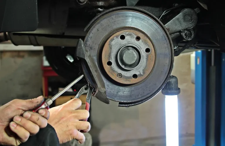 Mechanic inspecting a car's brake rotor and new pads in a repair bay