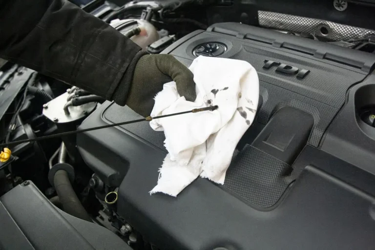 Mechanic checks engine oil under the hood of a sedan in a sunlit service bay