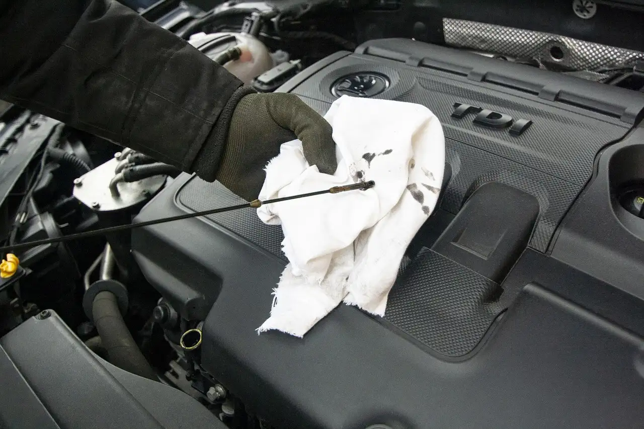 Mechanic checks engine oil under the hood of a sedan in a sunlit service bay