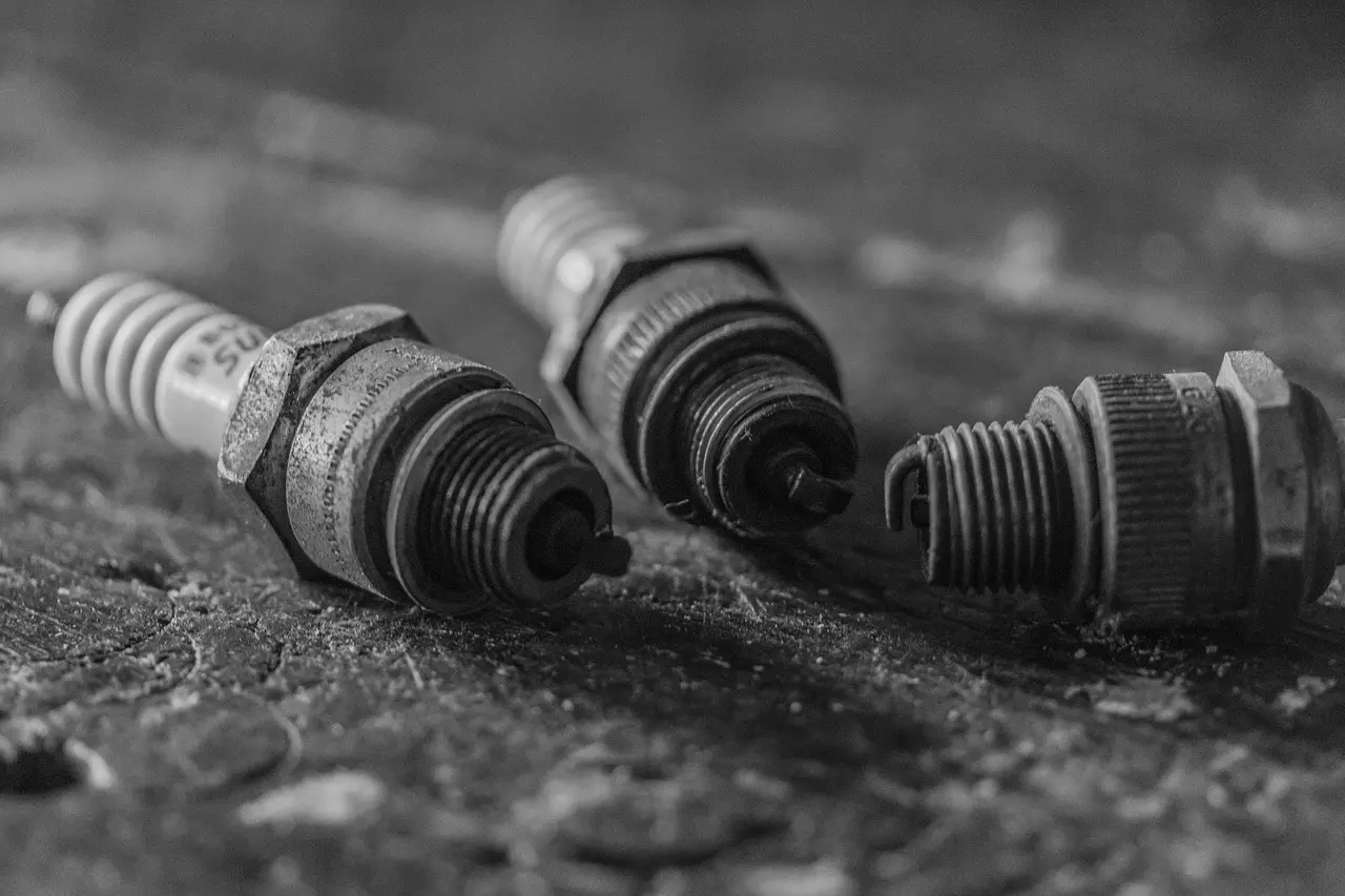 Mechanic examining worn spark plugs beside an open engine bay in a garage.
