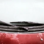 Person comparing windshield wiper blades beside a wet car windshield